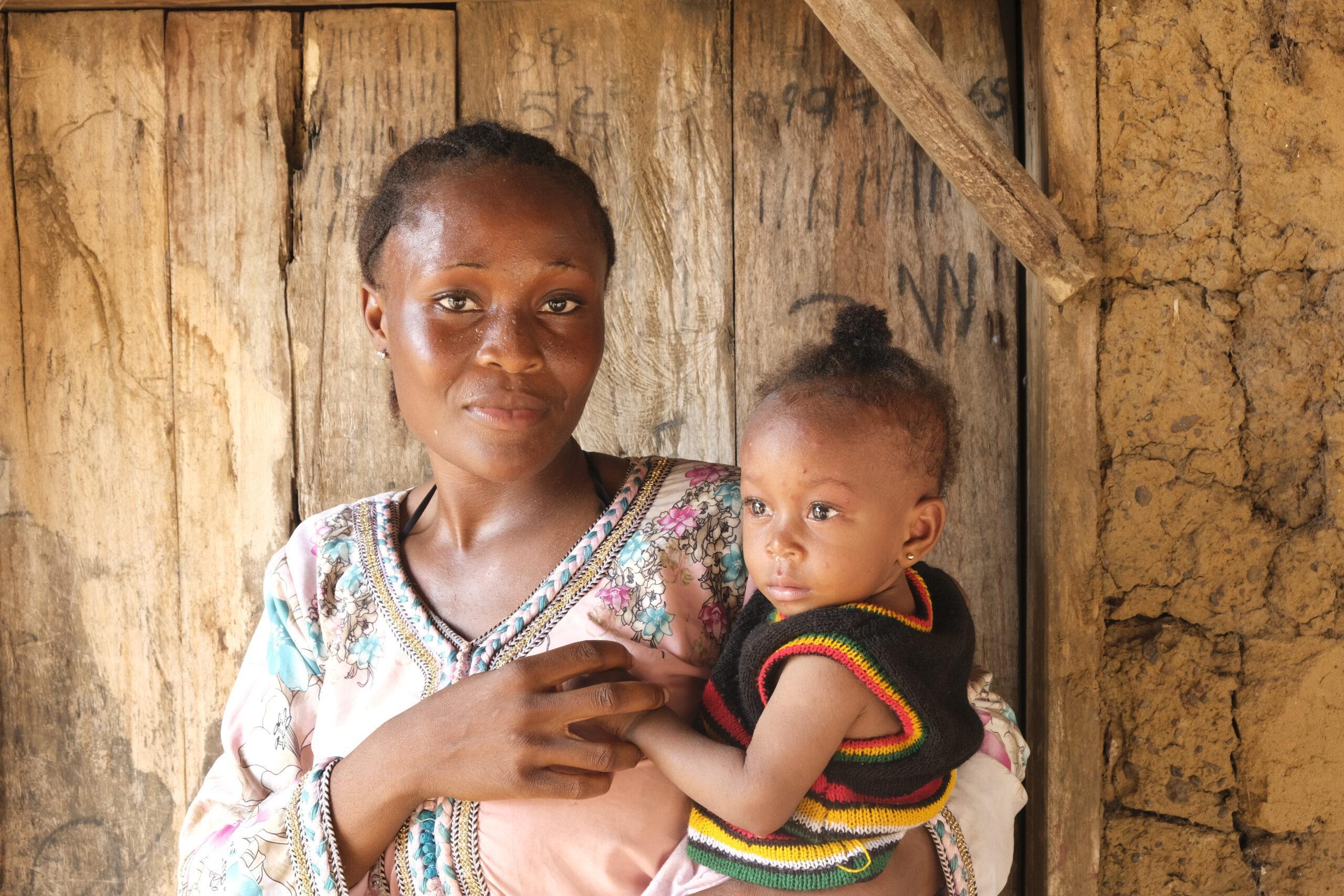 Junge afrikanische Frau, die sich gegen weibliche Gentialverstümmelung ausspricht, mit ihrem Baby auf dem Arm vor einer Holztür